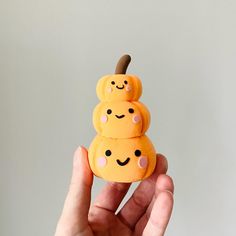 a hand is holding two small oranges with smiley faces on them and a wooden stick sticking out of the top