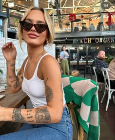 a woman sitting at a table with tattoos on her arm