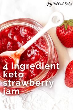 strawberry jam in a glass jar with a spoon and strawberries next to it on a white tablecloth