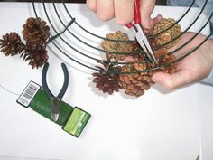 someone using scissors to cut pine cones on a wire wreath with twine and needles