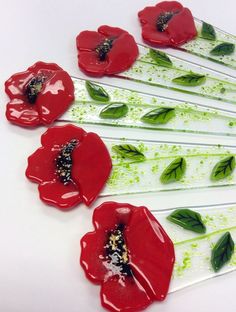 six red flowers are arranged on sticks with green leaves and sprinkles in the center