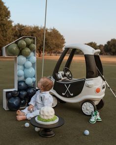 a baby is sitting in front of a golf cart with balloons on the ground behind it