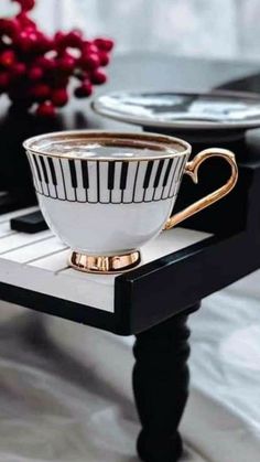 a black and white coffee cup with gold rim on a piano keyboard table next to a red flower