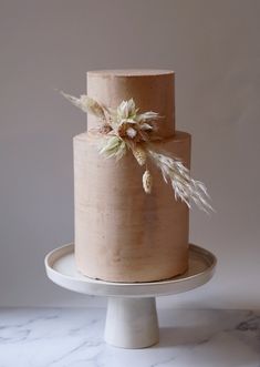 a three tiered cake with flowers and feathers on the top is sitting on a plate