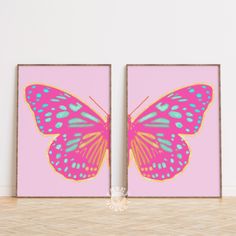 two pink and blue butterfly paintings against a white wall in an empty room with wood flooring