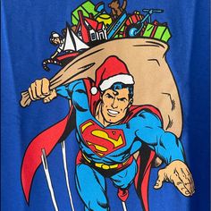 a man in a santa hat carrying a sack of gifts on his back and wearing a superman t - shirt