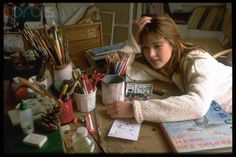 a woman sitting at a desk with lots of pens and pencils in her hand