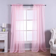 a white chair sitting in front of a window with pink curtains on the windowsill