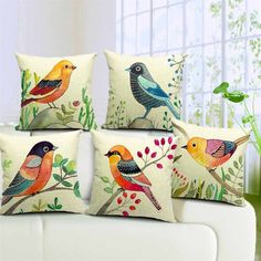 four colorful birds sitting on top of pillows in front of a white couch with green plants