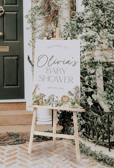 a welcome sign in front of a green door with greenery on it and the words,'welcome to victoria's baby shower '