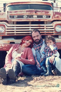 a man, woman and child sitting in front of an old truck