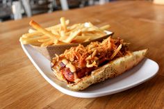 a hot dog and french fries on a white plate with a wooden table in the background