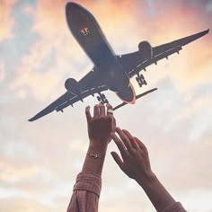 two people reaching up to an airplane in the sky with their hands on each other