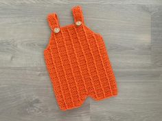 an orange crocheted baby bib laying on top of a wooden floor next to a pair of scissors