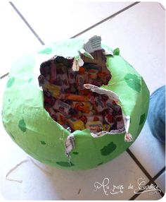 a green paper mache filled with candy sitting on top of a tiled floor next to a persons leg