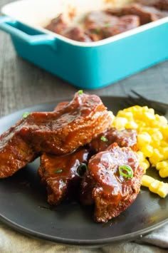 two pieces of meat with sauce and corn on a black plate next to a blue container