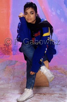 a young woman sitting on top of a wooden block wearing white sneakers and a blue sweater