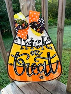 a trick or treat sign hanging from a wooden porch railing with a bow on it