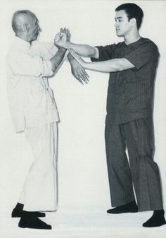 two men standing next to each other in front of a white wall with one holding the hand of another man