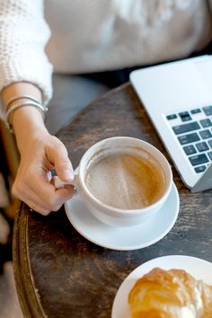 a person is sitting at a table with a cup of coffee and a croissant