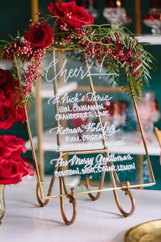 a sign that has some flowers on it with wine glasses in front of it and red roses