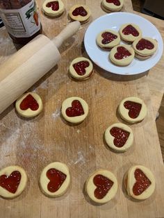 heart shaped cookies sitting on top of a wooden cutting board next to a rolling pin