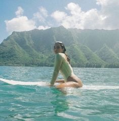 a woman is sitting on a surfboard in the middle of the ocean with mountains in the background