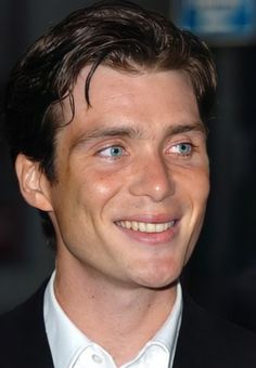 a close up of a person in a suit and tie smiling at the camera with blue eyes