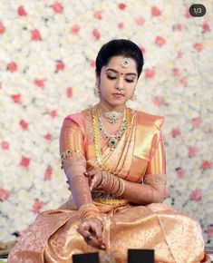 a woman sitting on the ground wearing a gold and red sari with jewelry in her hands