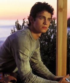 a young man sitting at a table with a laptop computer in front of him and looking off into the distance