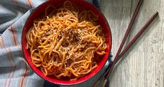 a red bowl filled with noodles and chopsticks on top of a wooden table