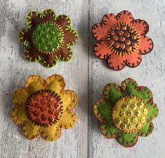 four flower brooches sitting on top of a white wooden table next to each other