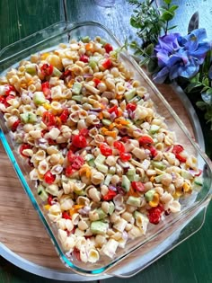 a casserole dish filled with pasta and vegetables on a wooden tray next to flowers