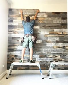 a man standing on top of a step ladder in front of a wall made out of wood planks