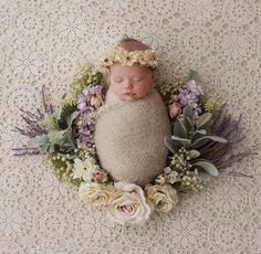 a newborn baby wrapped in a blanket surrounded by flowers and greenery on a crocheted doily