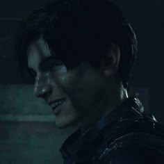 a man with dark hair and leather jacket looking to his left in a dimly lit room