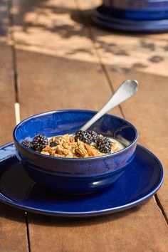 a blue bowl filled with oatmeal and berries on top of a plate