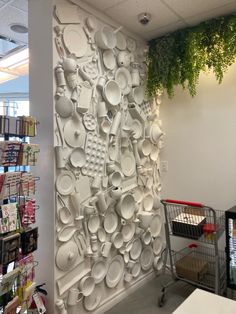 a wall covered in lots of white plates and pans next to a shopping cart