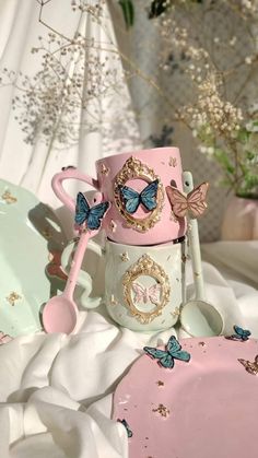 a pink and white coffee mug with butterflies on the top, sitting next to a spoon