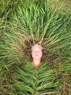 a woman is hiding in the grass with her head hidden behind some tall green plants