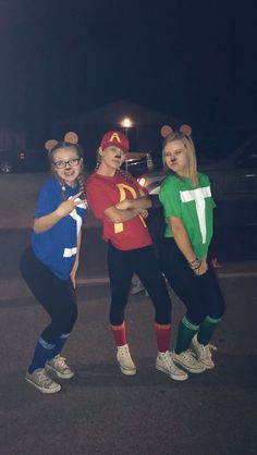 three women in costumes standing next to each other on the street at night with their arms around one another