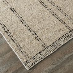 a beige rug with black lines on the top and bottom, laying on a wooden floor