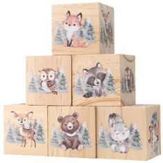 four wooden blocks with pictures of animals and pine trees on them, all painted in different colors