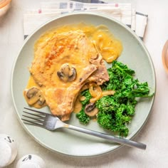 a white plate topped with meat covered in gravy and broccoli next to an egg