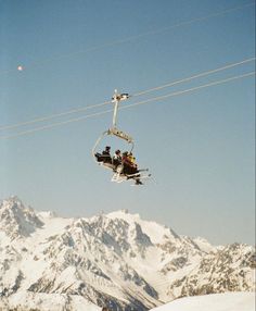 two people riding a ski lift in the air above snow covered mountains and power lines