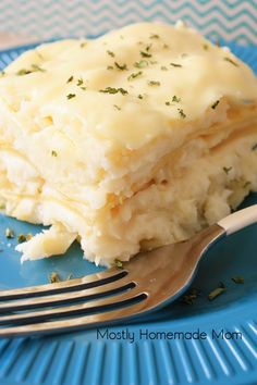 a blue plate topped with mashed potatoes covered in cheese and herbs next to a fork