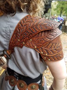 the back of a woman's leather vest with leaves on it and buttons at the waist