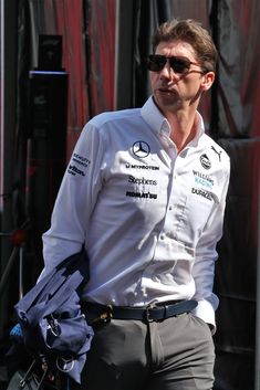 a man in white shirt and sunglasses walking down the street with his hand on his hip