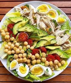 a white plate topped with lettuce, tomatoes and chickpeas next to hard boiled eggs