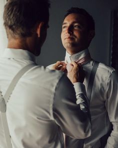 a man adjusting his bow tie in front of another man who is looking into the mirror